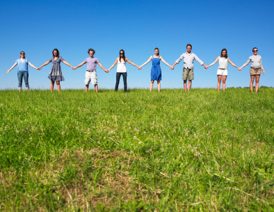 Group of friends holding hands in meadow under blue sky