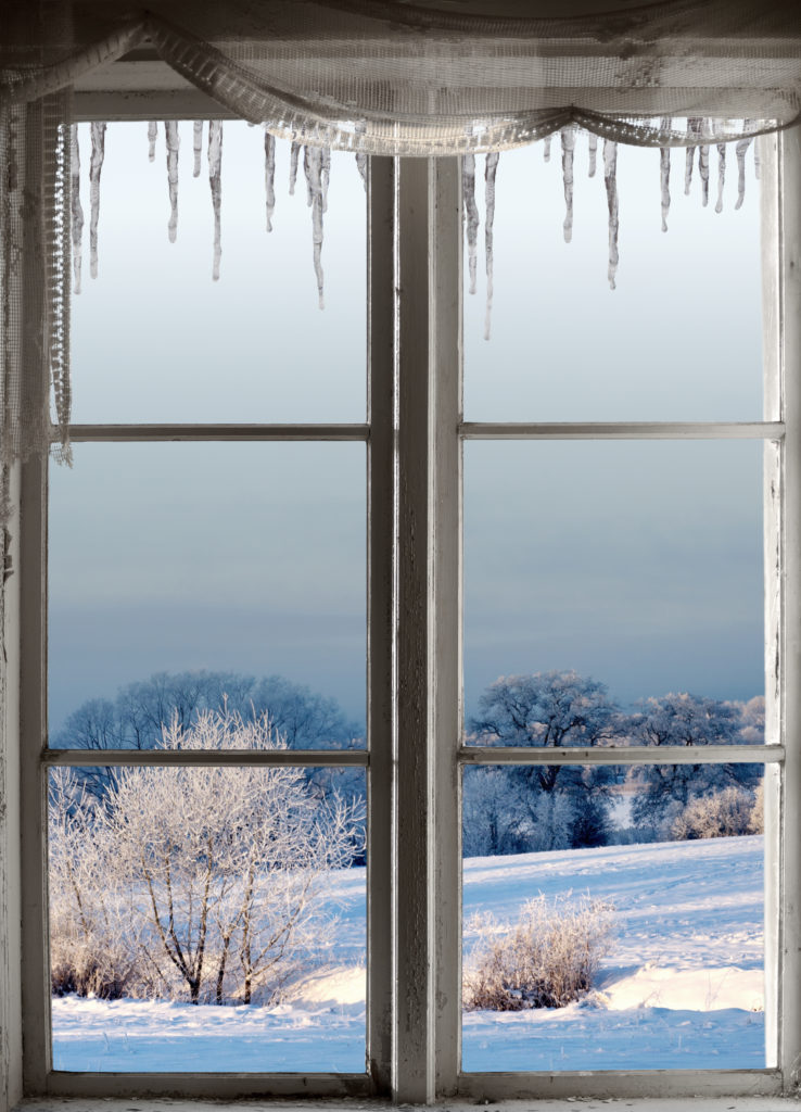 Beautiful winter landscape with rime frost in bushes and trees, seen through an old window with icicles
